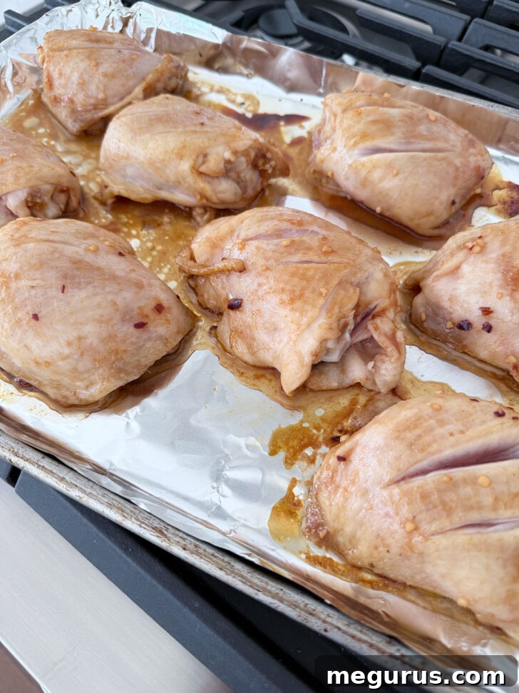 Partially cooked chicken thighs on the baking sheet.