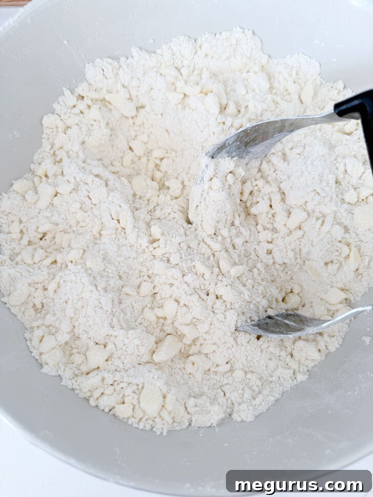 Cutting the cold butter into the flour mixture with a pastry cutter until pea-sized crumbs form.