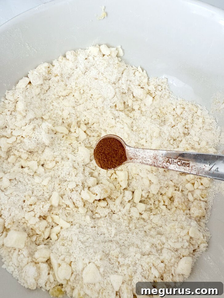 Cinnamon being added to the reserved crumb mixture in a bowl.