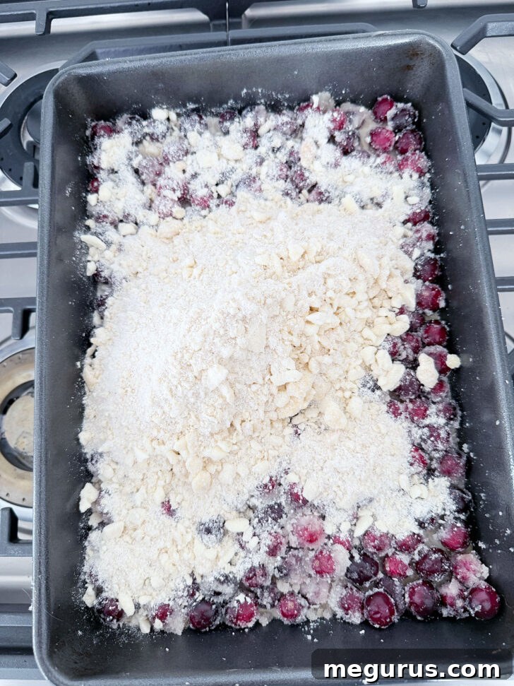 Remaining spiced crumb topping being scattered over the cranberry filling.