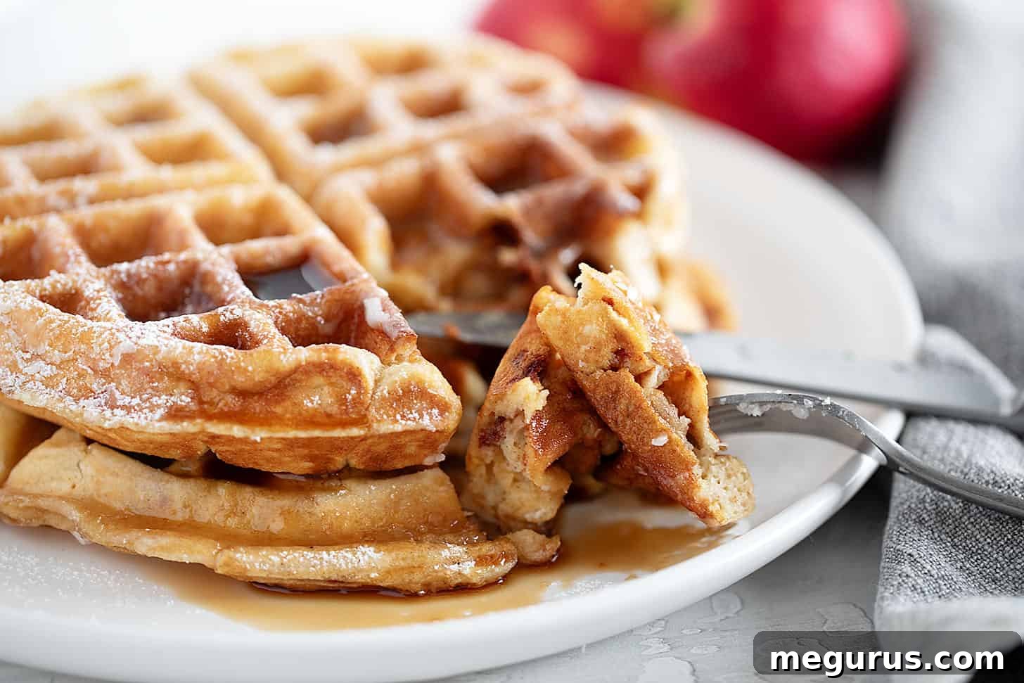 Golden brown Apple Fritter Waffles served on a plate with a fork, drizzled with sweet glaze and ready to be enjoyed.