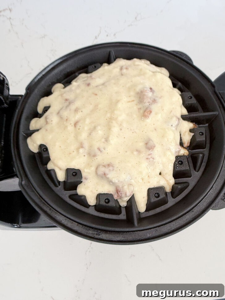 A scoop of apple fritter waffle batter carefully poured onto a hot, preheated waffle iron, ready to cook.