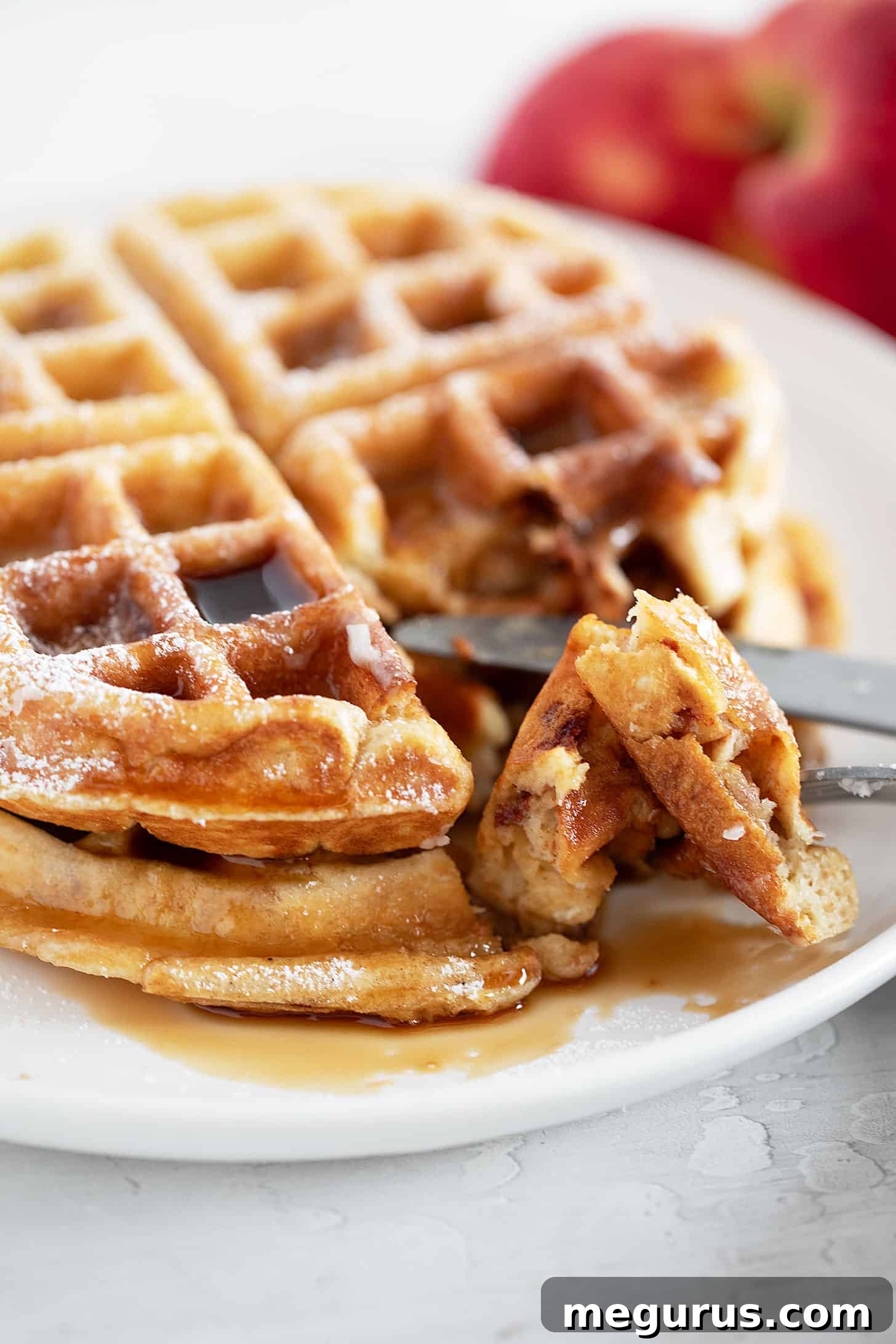 A close-up of a beautifully glazed Apple Fritter Waffle on a plate, with delicate glaze drips and perfectly cooked apples visible, ready to be enjoyed.