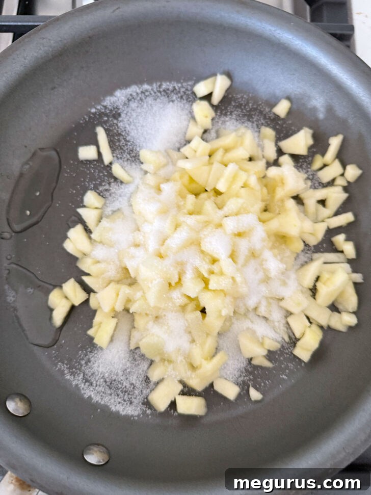 Diced tart apples, white sugar, and lemon juice in a skillet before cooking, ready to be stirred.