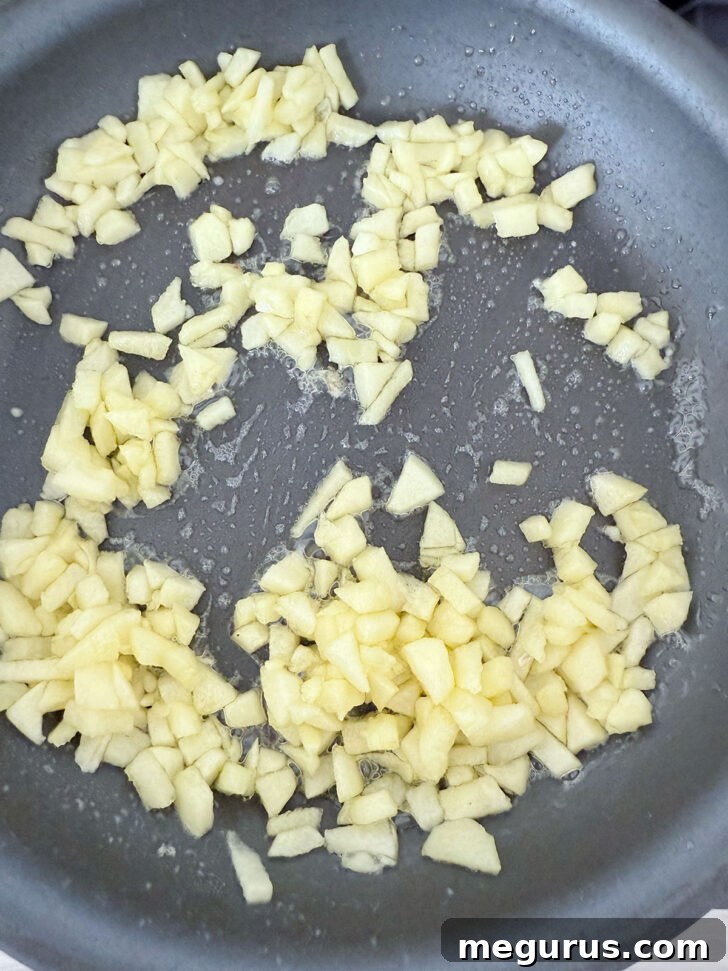 Apples cooking in a skillet over medium heat, softening and releasing their natural liquid, which is beginning to evaporate.