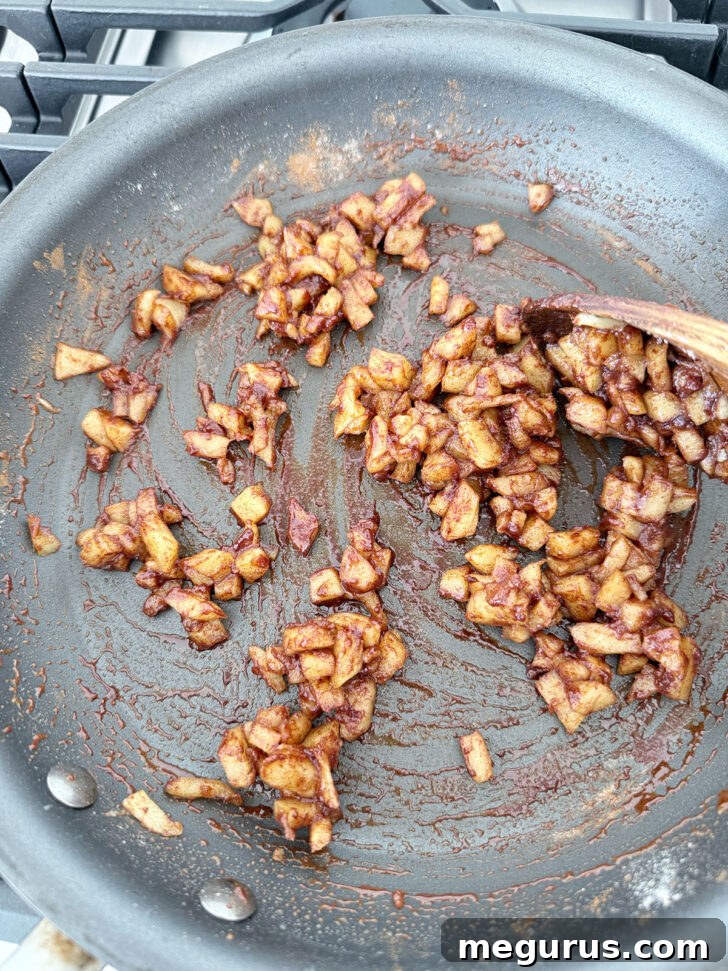 Ground cinnamon and all-purpose flour being stirred into the softened apples in the skillet, coating them evenly.