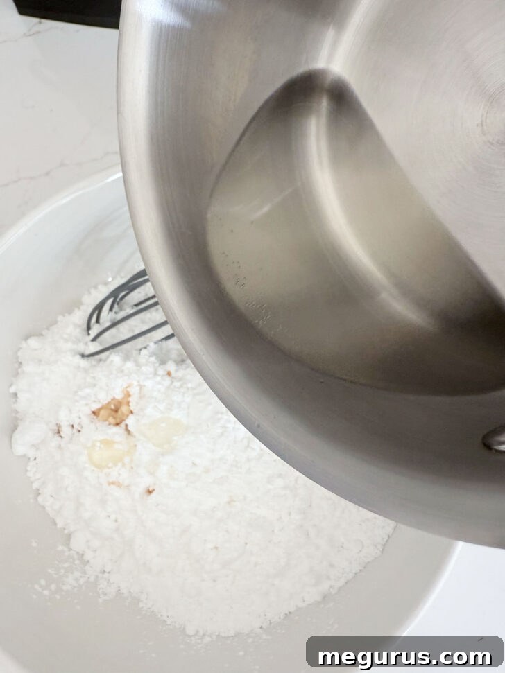 Hot, clear sugar syrup being carefully poured into a bowl of white icing sugar, ready to be whisked into a glaze.