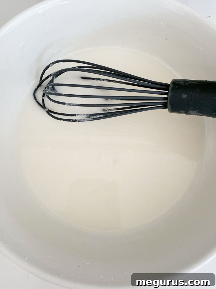 The finished, smooth, and glossy apple fritter glaze resting in a bowl with a whisk, ready for application.