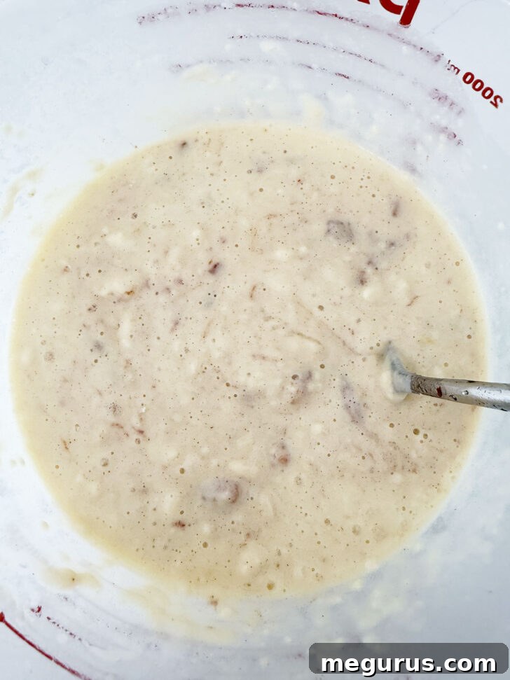 The finished apple fritter waffle batter, with cinnamon-coated apple pieces evenly distributed, resting in a bowl, ready to be cooked.
