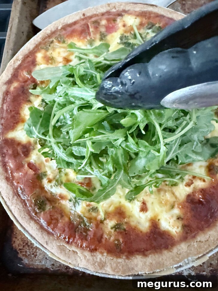 Placing the dressed arugula topping onto the cooked quiche.
