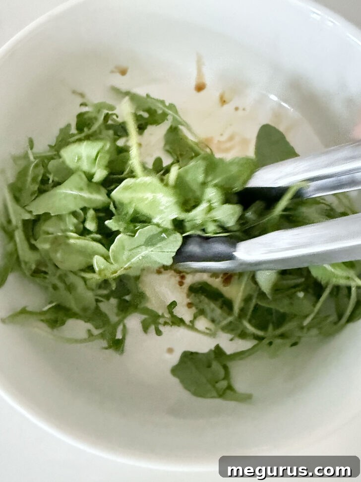 Tossing arugula topping in a bowl with dressing.