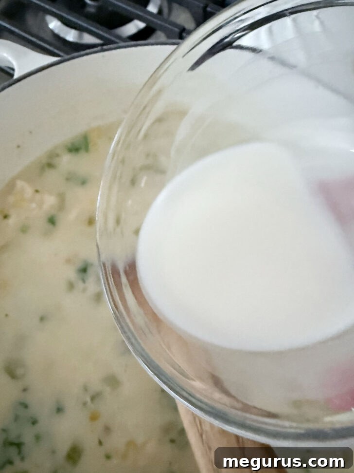 Adding a cornstarch slurry to thicken the cod chowder to desired consistency.