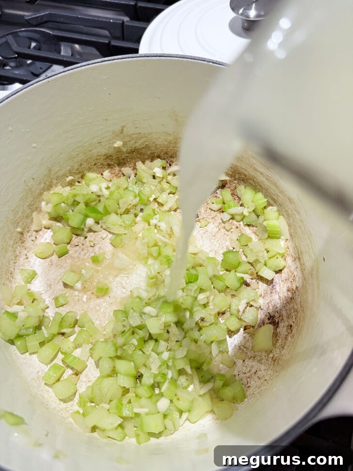 Pouring broth into a pot with cooked onion and celery.