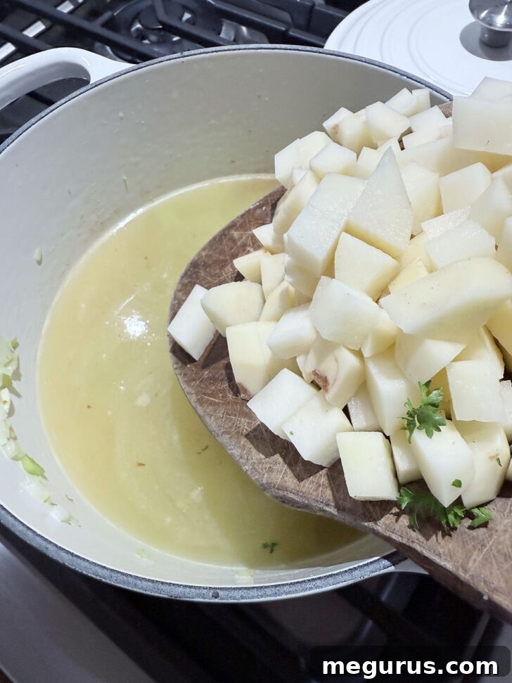 Adding diced potatoes to the simmering broth in a soup pot.