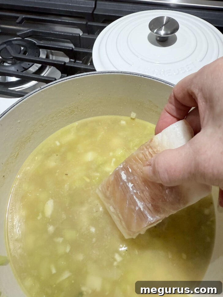 Adding frozen cod pieces to the bubbling chowder broth.