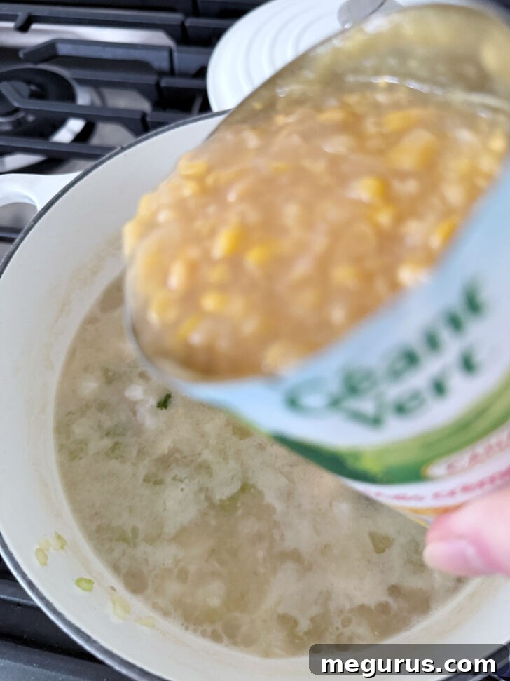 Stirring in a can of creamy corn into the cod chowder.