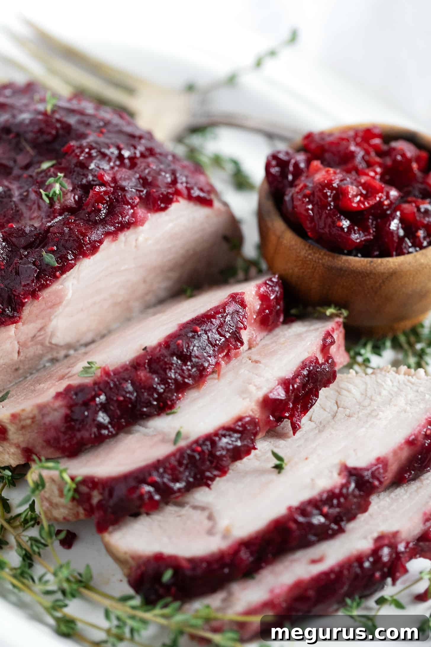 Cranberry apple glazed pork roast sliced on a serving plate, garnished with fresh herbs.