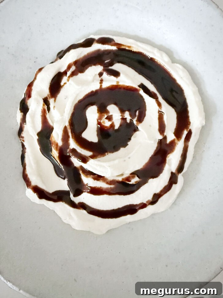 Thick balsamic glaze artfully drizzled over the smooth whipped ricotta in a bowl.