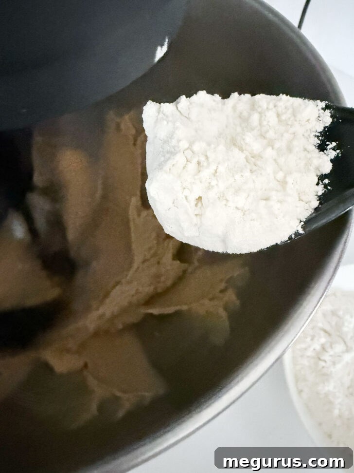 Dry flour mixture being gently incorporated into the wet cookie dough in a mixer bowl.