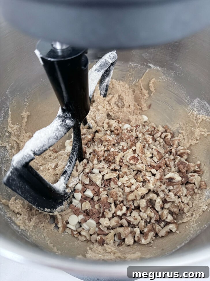 Toffee bits, white chocolate chips, and chopped walnuts being folded into the prepared cookie dough.