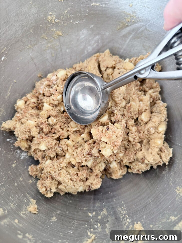 A large cookie scoop being used to portion out uniform balls of cookie dough onto a baking sheet.
