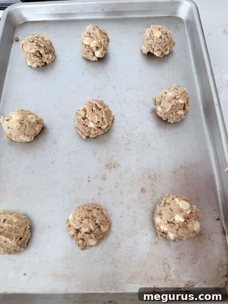 Portioned cookie dough balls, spaced appropriately on a parchment-lined baking sheet, awaiting baking.