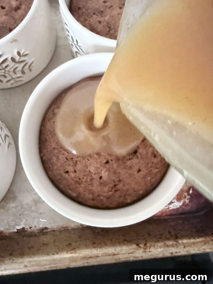 Warm toffee sauce being poured generously over the freshly baked gingerbread sticky toffee puddings in ramekins.