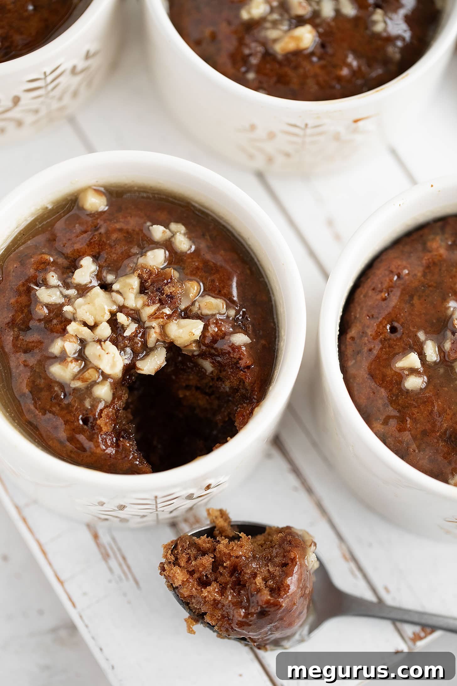 Two individual gingerbread sticky toffee puddings generously coated with rich toffee sauce and garnished with chopped nuts.