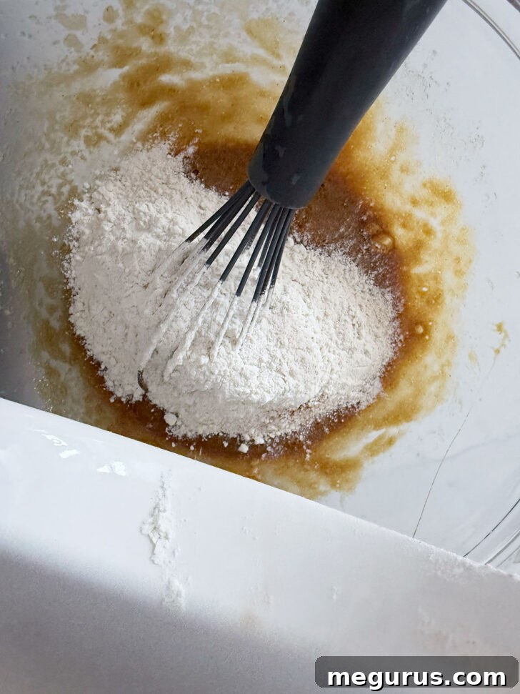 The whisked dry flour mixture being gently folded into the wet pudding batter.