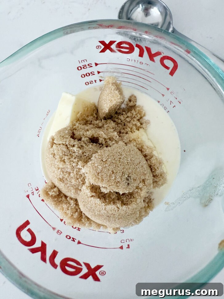 Ingredients for the toffee sauce, including butter, cream, and brown sugar, being measured into a glass measuring cup.