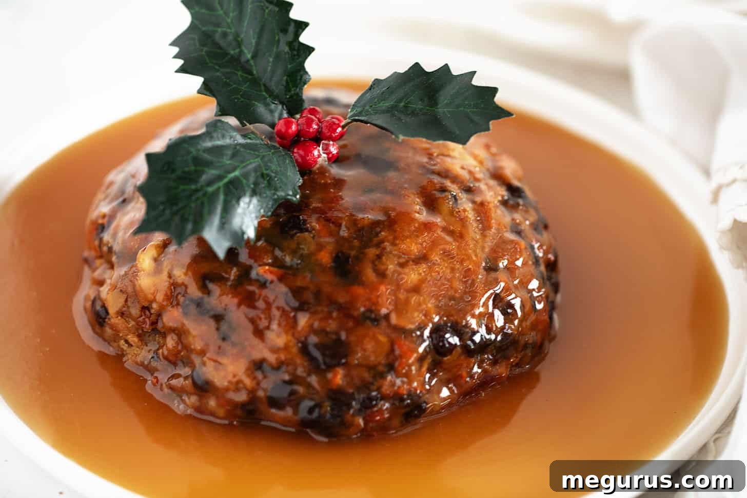 Christmas pudding with rum sauce on a serving plate, adorned with festive holly.