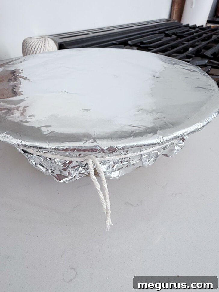 Pudding bowl covered with parchment paper and aluminum foil, tied with string.
