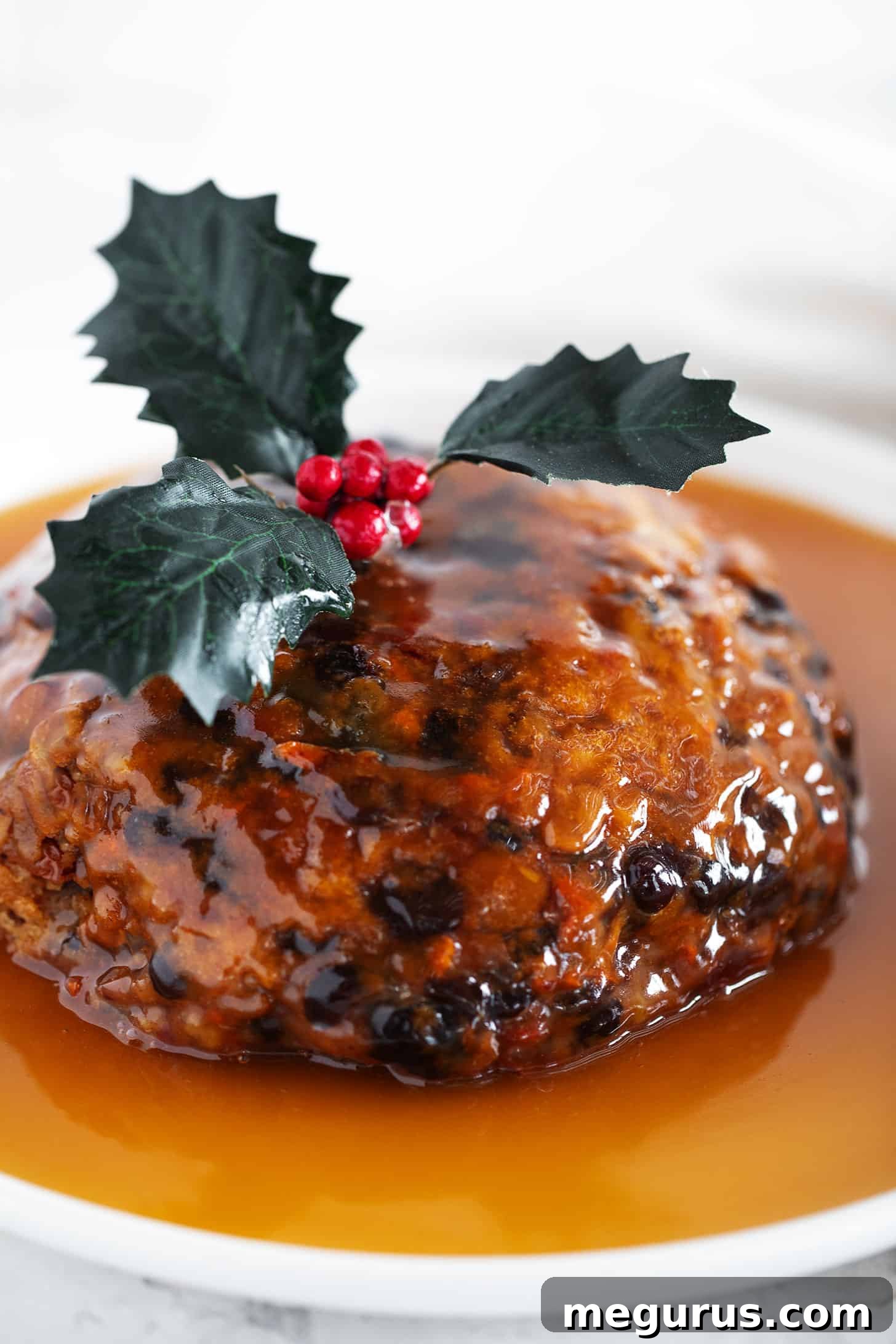Christmas pudding on a serving plate with a rich, glistening rum sauce poured overtop.