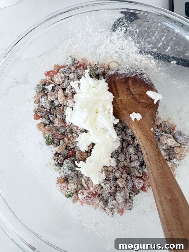 Grated frozen shortening being added to the bowl with dried fruit and dry ingredients.
