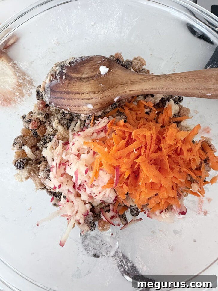 Grated apple and carrot added to the Christmas pudding mixture in a bowl.