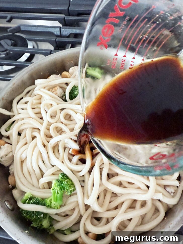 Adding the sauce to the skillet with the noodles, chicken, broccoli and cashews.