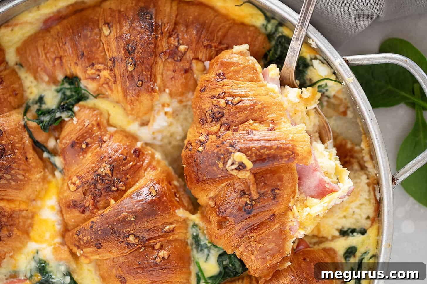 A golden, puffed ham and cheese croissant bake in a round baking dish, ready to serve.