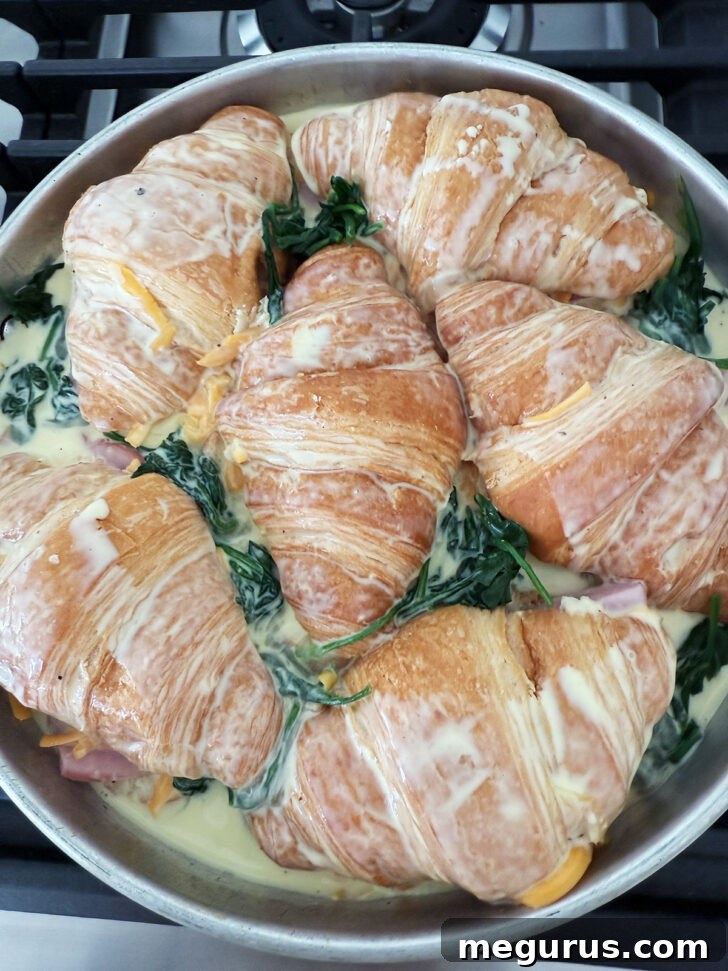 Pouring the egg custard mixture over the filled croissants in the baking dish.