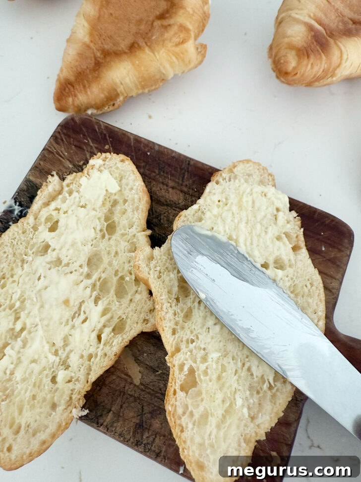 Buttering the interior of split croissants.