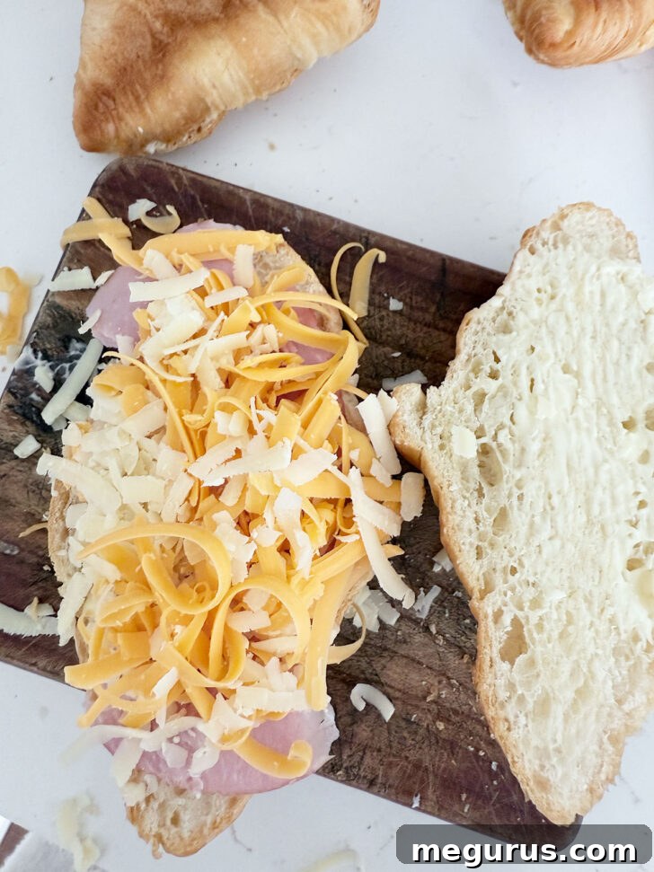 Layering ham and shredded cheese onto the bottom half of a croissant.