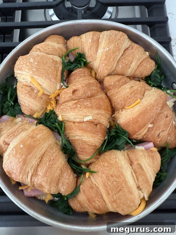 Scattering wilted spinach among the filled croissants in the baking pan.