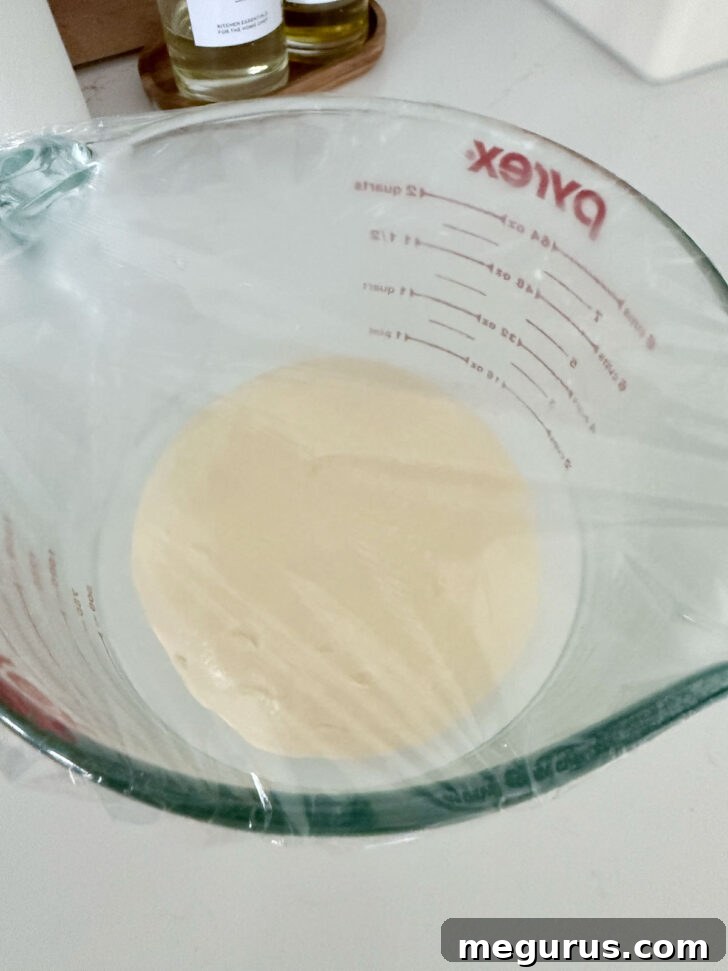 Greased dough ball placed in a large measuring cup, ready for the first rise.