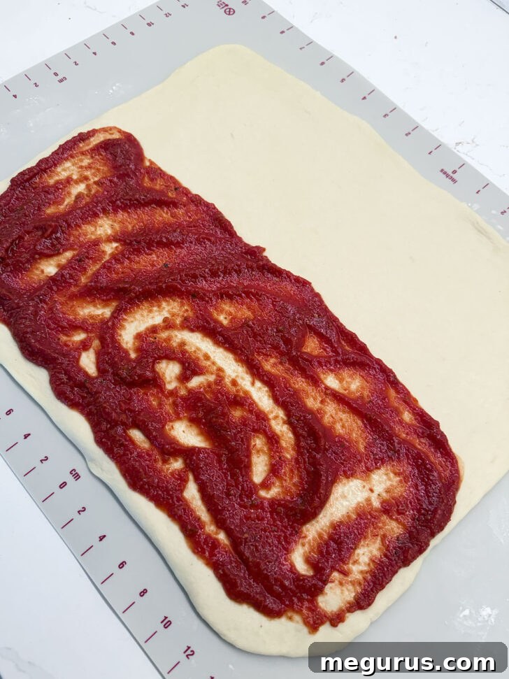Pizza sauce evenly spread over one half of the rolled-out dough rectangle.