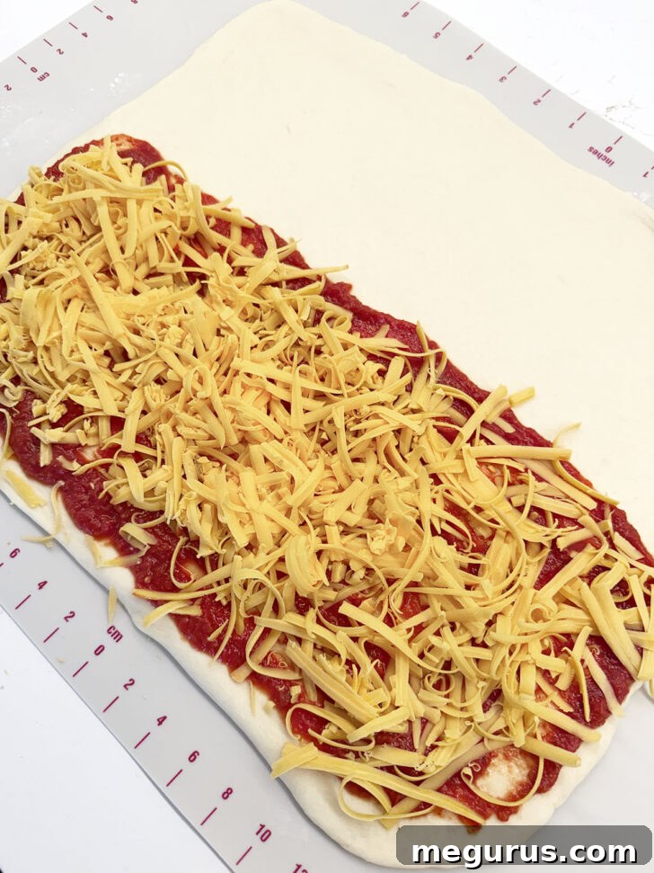 Generous layer of shredded cheese sprinkled over the pizza sauce.