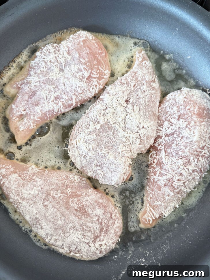 Parmesan-coated chicken cutlets cooking in butter and olive oil in a skillet.
