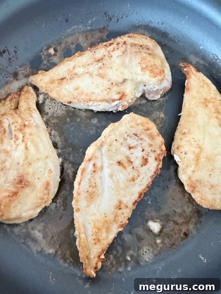 Golden-browned chicken cutlets in a skillet after searing on one side.