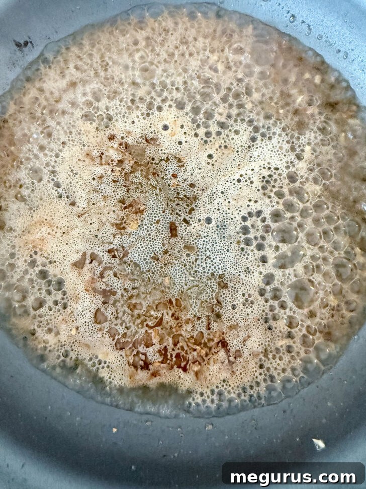 Skillet after white wine was added to deglaze, showing bubbling liquid and scraped-up bits.