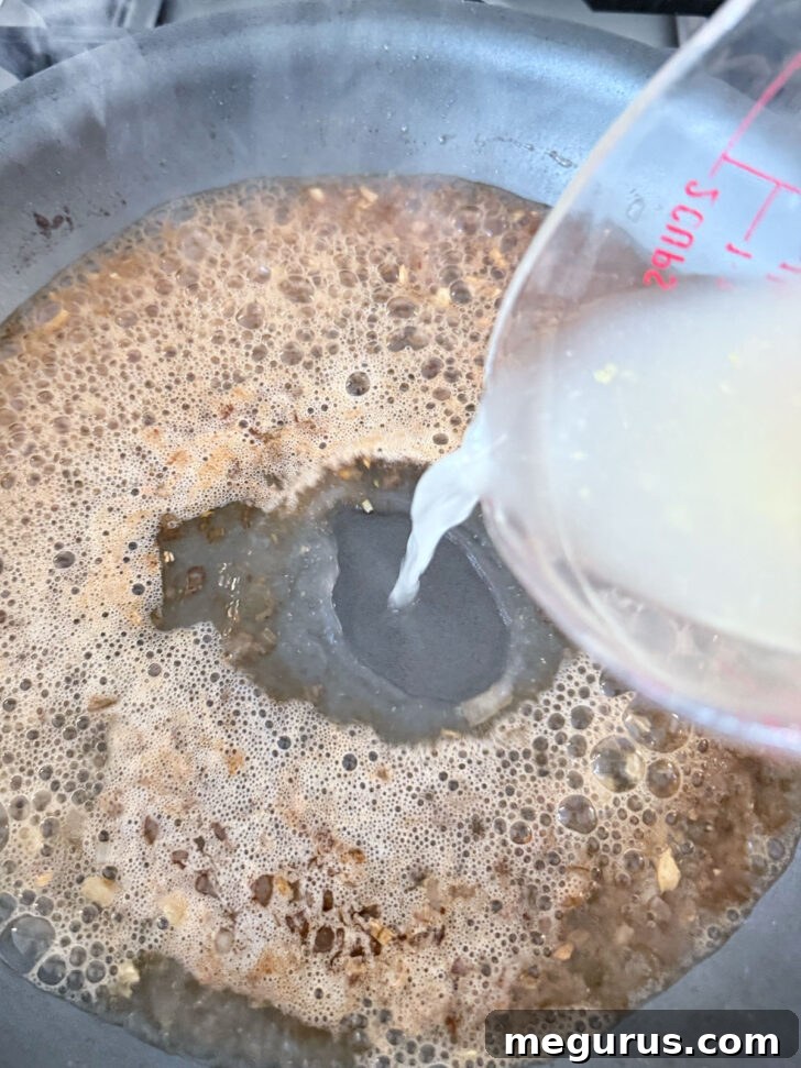 Adding chicken broth to the skillet with the deglazed wine and aromatics.