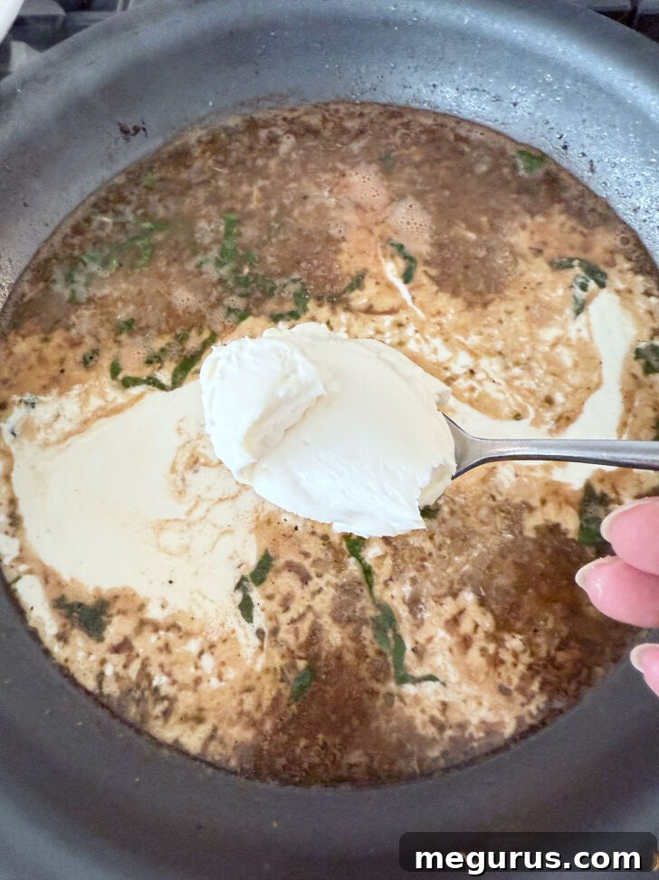 Adding heavy cream and softened cream cheese to the simmering sauce in the skillet.