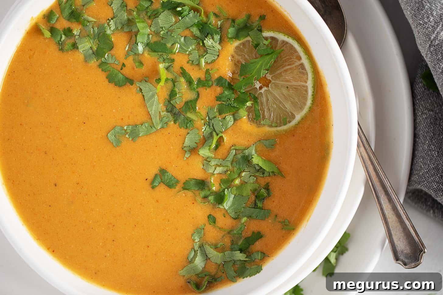 A vibrant bowl of sweet potato coconut curry soup, garnished with fresh herbs.